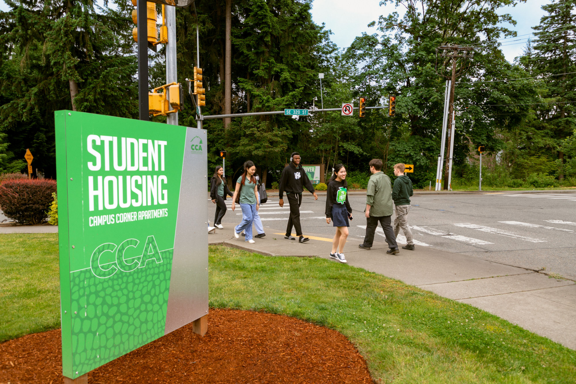 People walking in front of a sign that reads, Student Housing Campus Corner Apartments unit