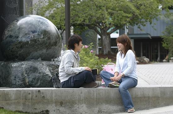photo of two Green River College students sitting near a water sculpture on campus.