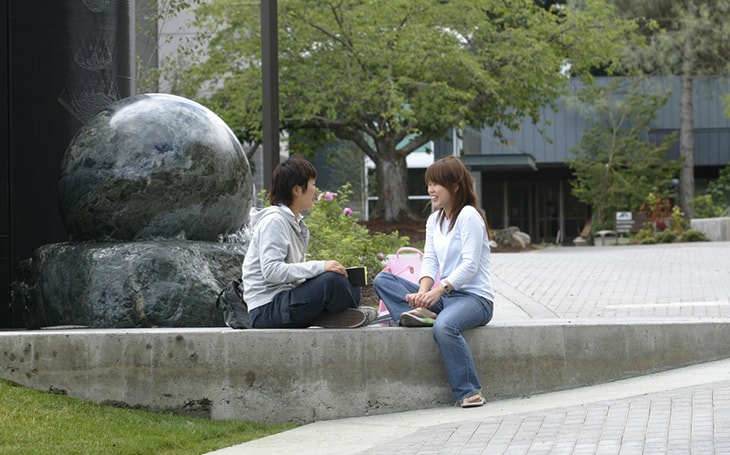 a photos of two students sitting near the water sphere sculpture