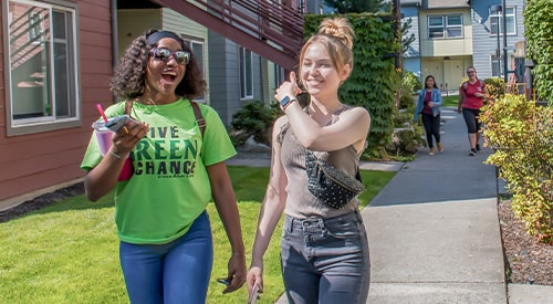 Two female Green River College students walking outside of Campus Corner Apartments on a sunny day.