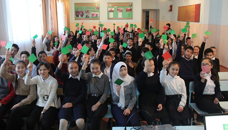 A group of school children holding up either red or green cards as part of a digital literacy training activity.