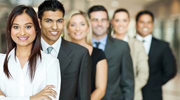 Six business professionals lined up behind one another smiling at the camera.