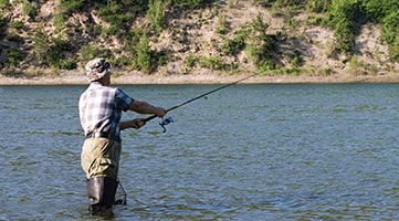 A fly fisherman casing a fishing line while standing in a river.