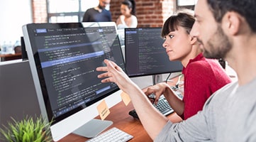 Photo of two computer programmers looking at code on a computer screen.