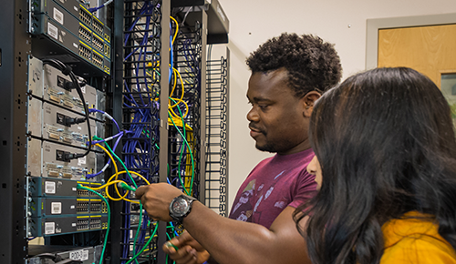 Two students working with a rack of electronics